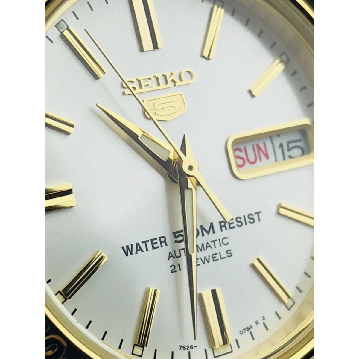 Seiko white dial close-up with gold hands, Water Resist, and SUN 15 day-date window