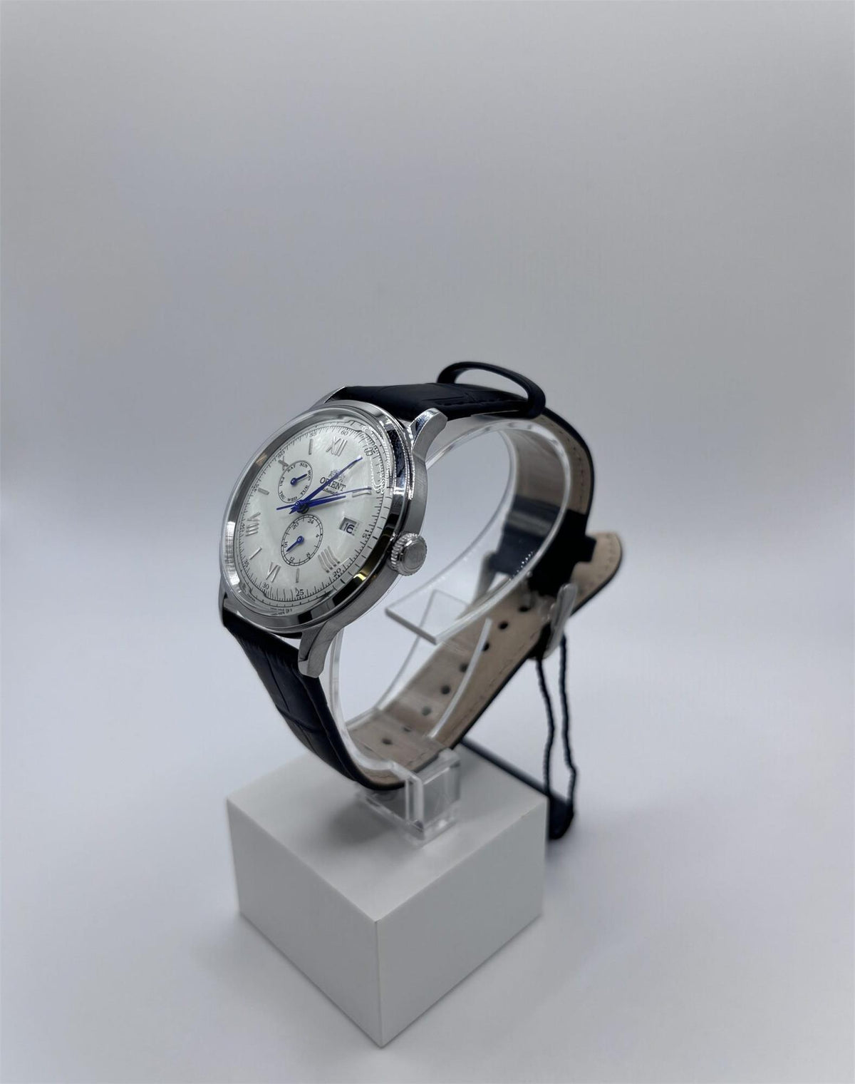 Men's automatic wristwatch with black leather strap, white dial, blue hands, on a stand.