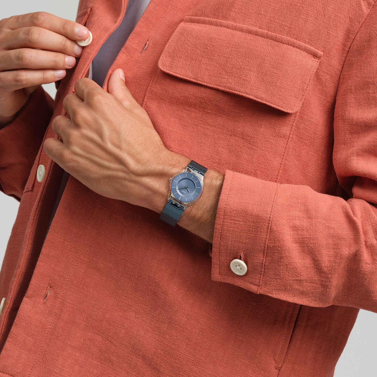 Men’s wristwatch on dark blue mesh strap worn with a rust-red button-up sleeve