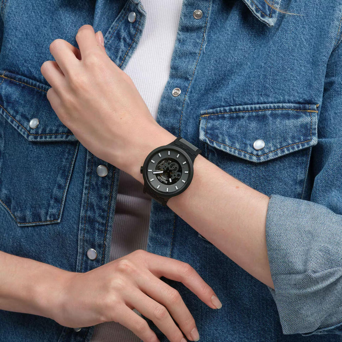 Men's black quartz watch on wrist with black rubber strap and dark skeleton dial.