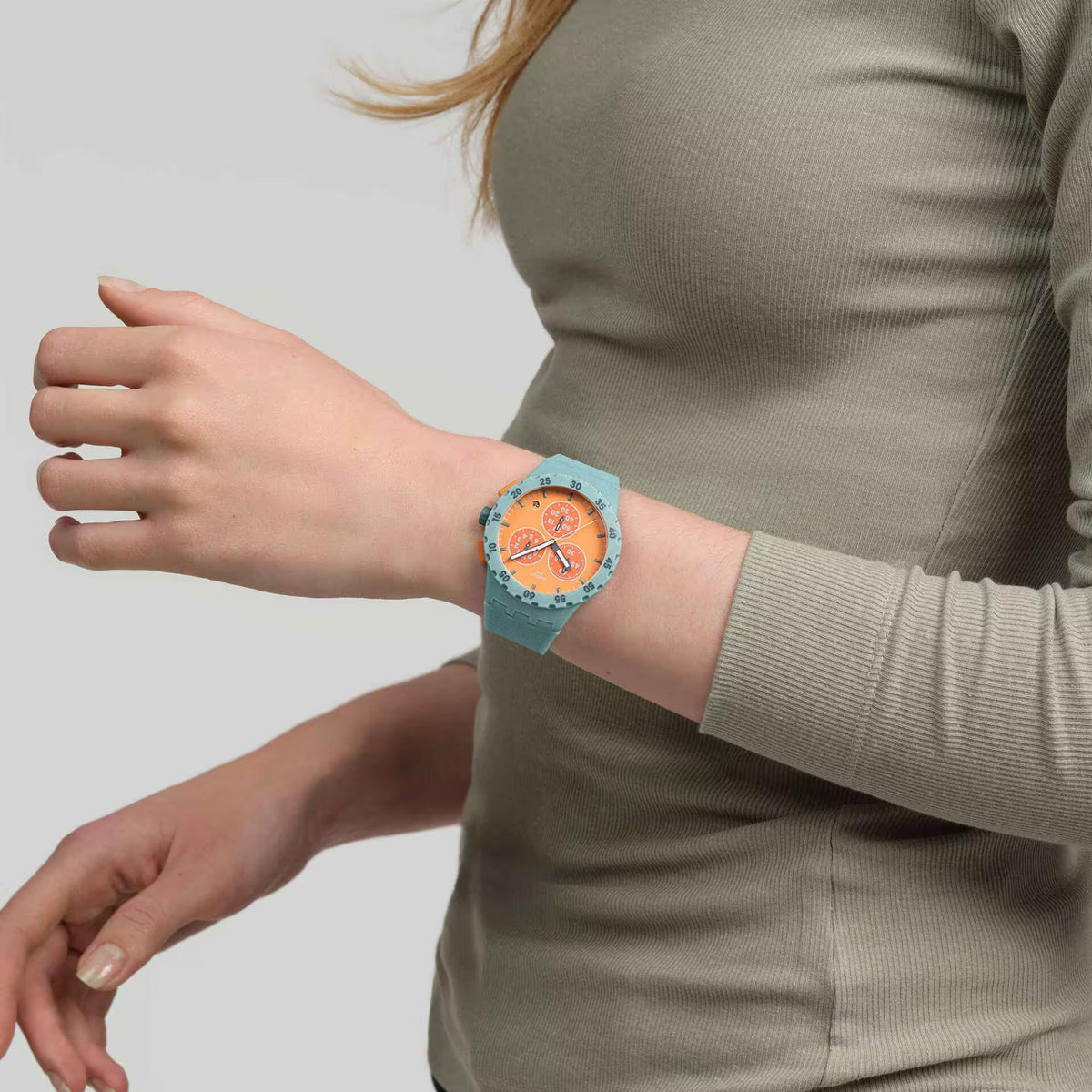 Quartz orange dial watch with teal silicone strap on arm, multiple orange time markers