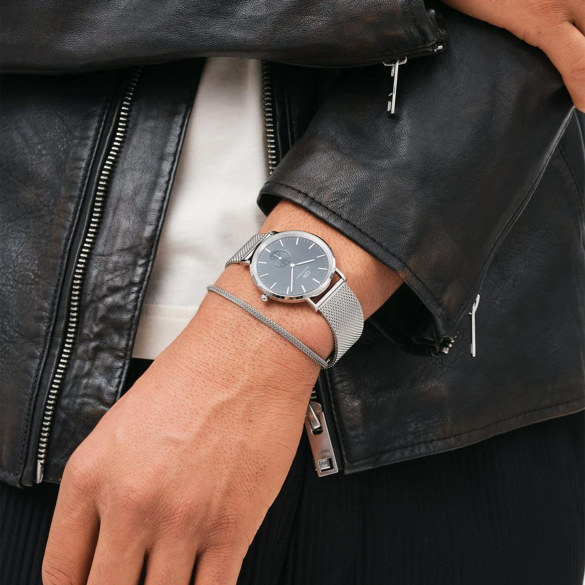 Daniel Wellington mens quartz watch on wrist with steel mesh bracelet and dark dial.