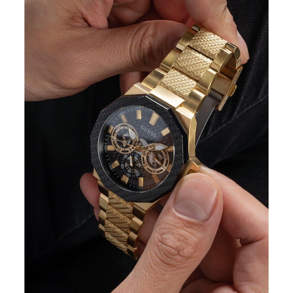 Two-tone men’s wristwatch on wrist; black dial with gold hands and three subdials, gold bracelet.