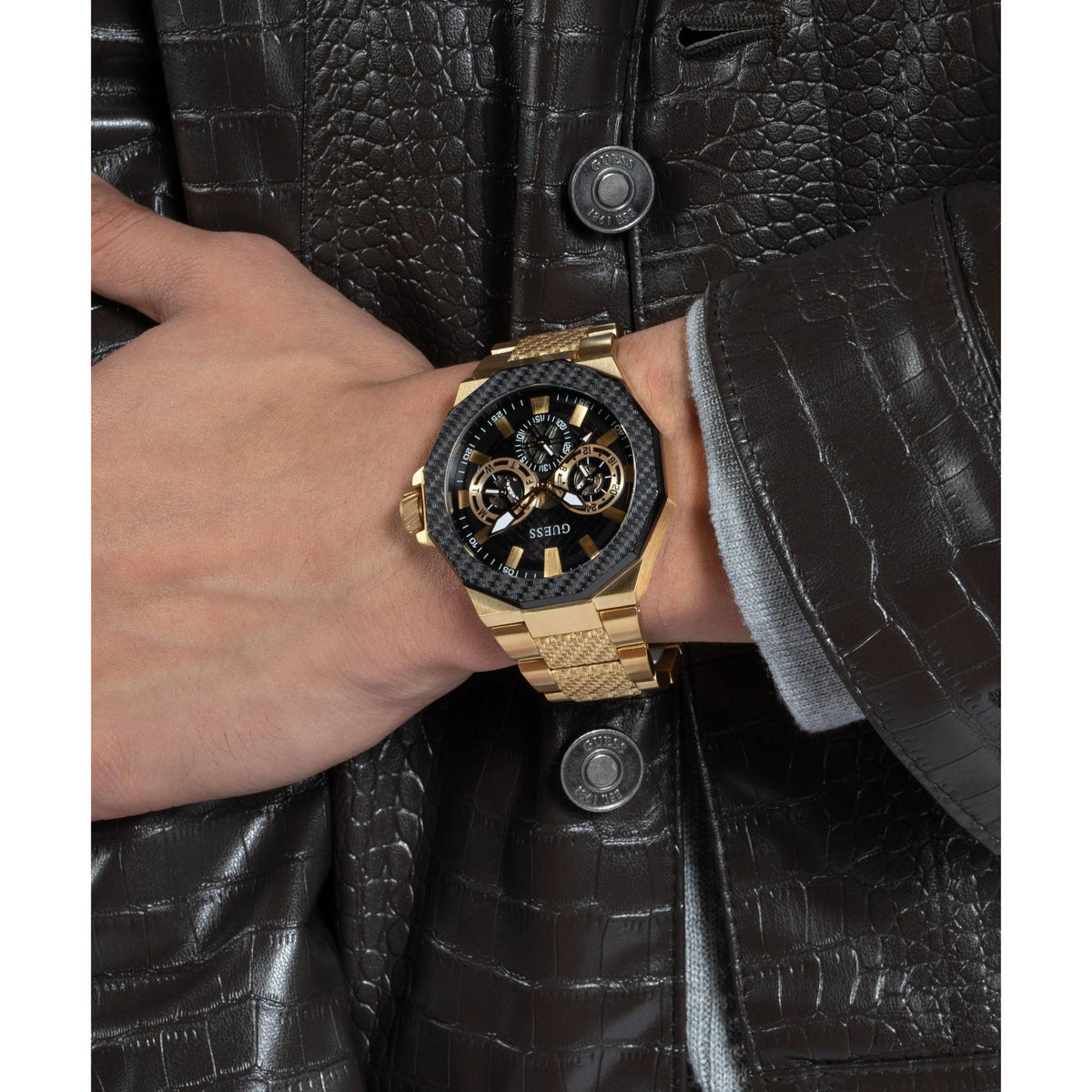 Two-tone men’s wristwatch on wrist; black dial with gold accents and gold-tone textured bracelet.