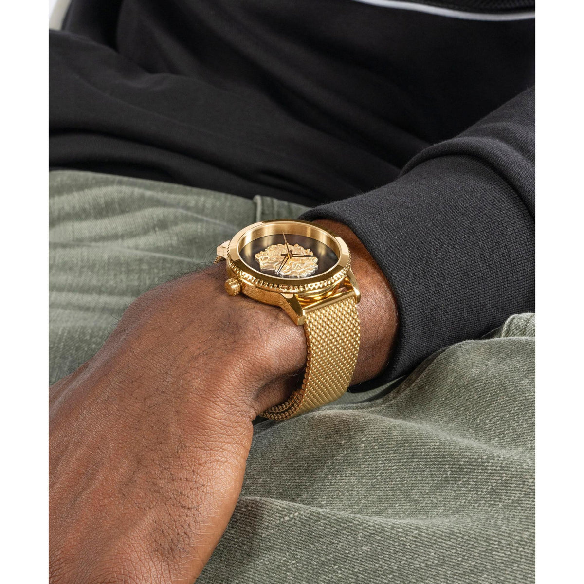 Gold-tone analog men's watch on wrist with black dial, lion medallion, and mesh bracelet