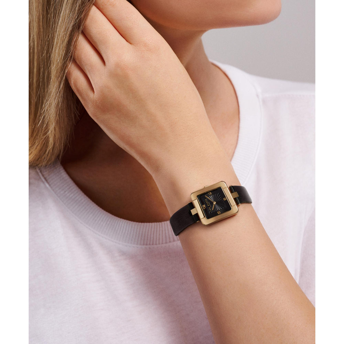 Square black dial watch with black leather strap on wrist, gold-tone bezel