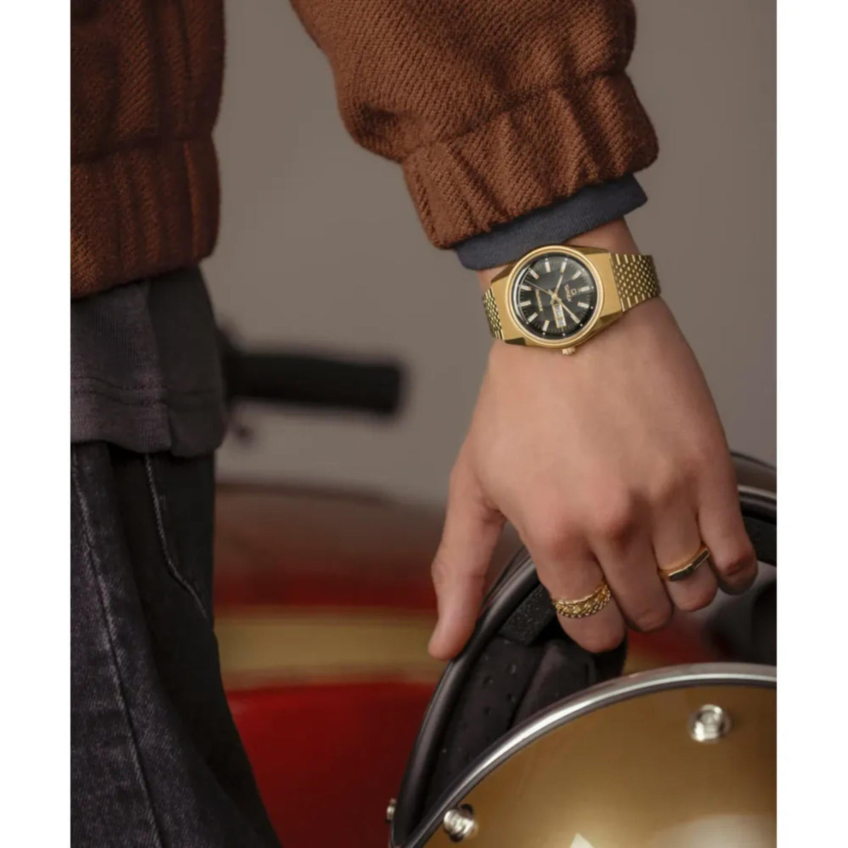 Gold-toned metal watch on wrist with dark dial and bracelet