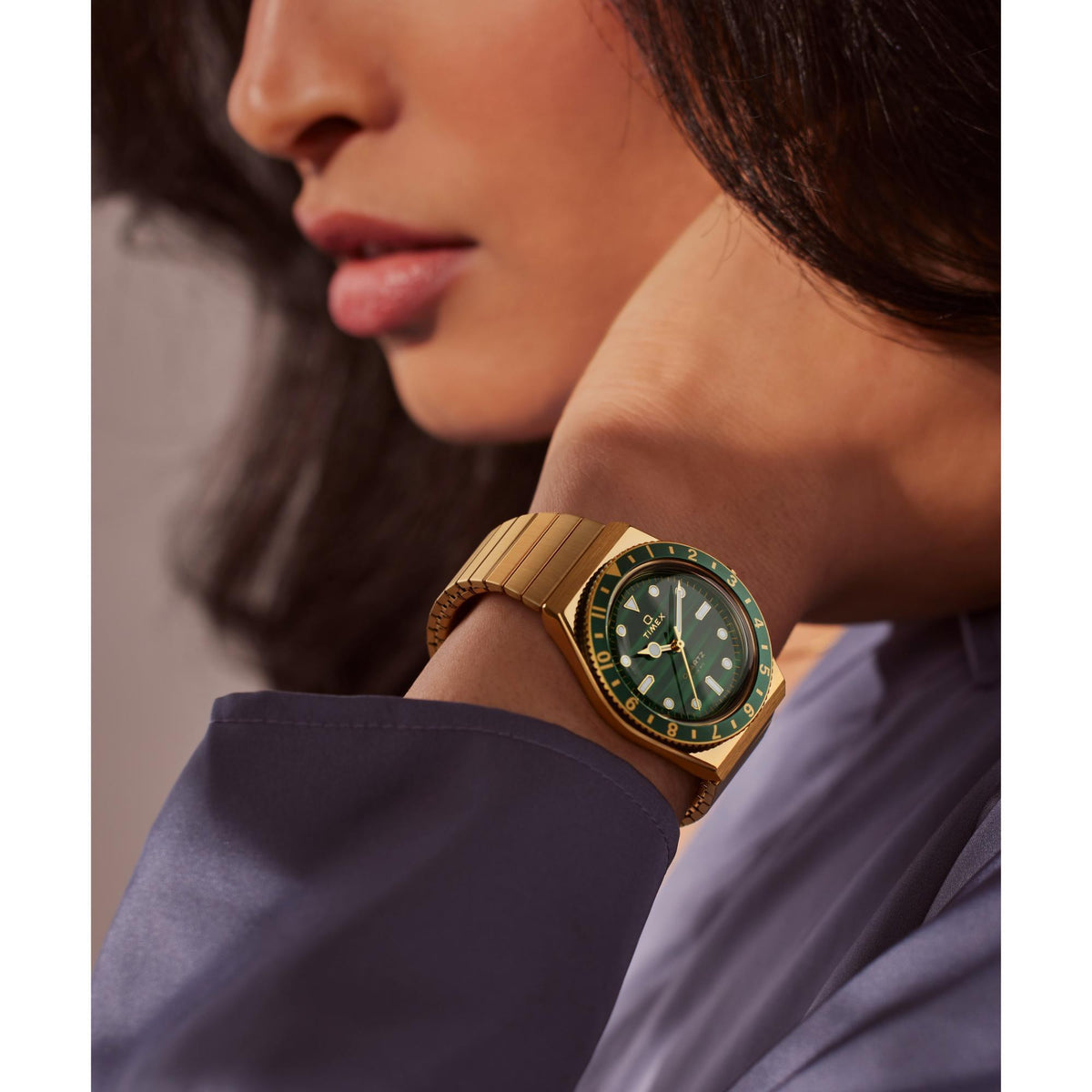 Green dial gold-tone steel quartz watch on wrist with metal bracelet