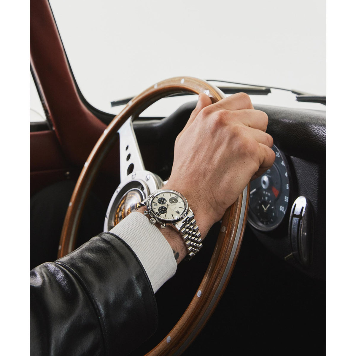 Men's silver steel Timex chronograph quartz watch on wrist with leather jacket, steering wheel visible