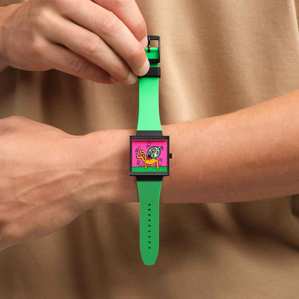Women’s watch on wrist: square black case, pink graphic dial, green silicone band