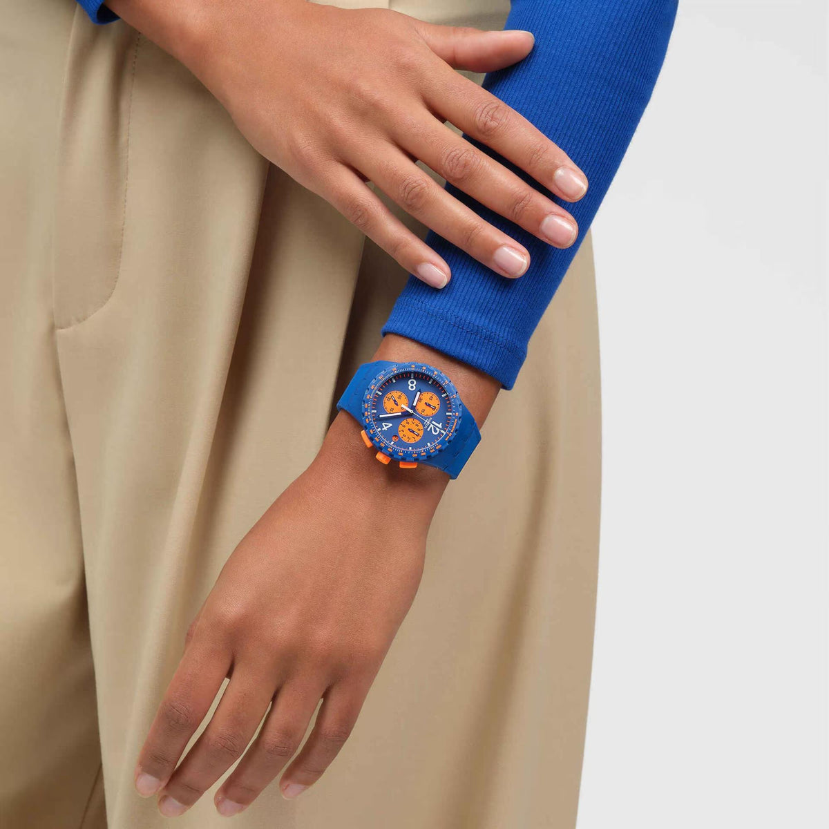 Man’s wrist wearing a blue chronograph watch with orange dial and silicone strap