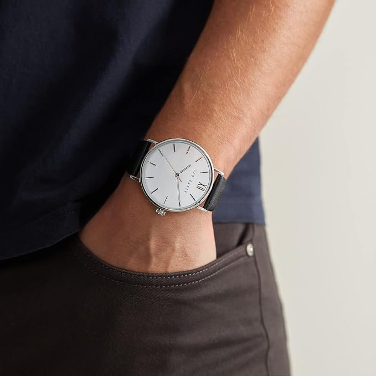 Men's wrist watch on wrist, black leather strap, white dial with slim hour markers