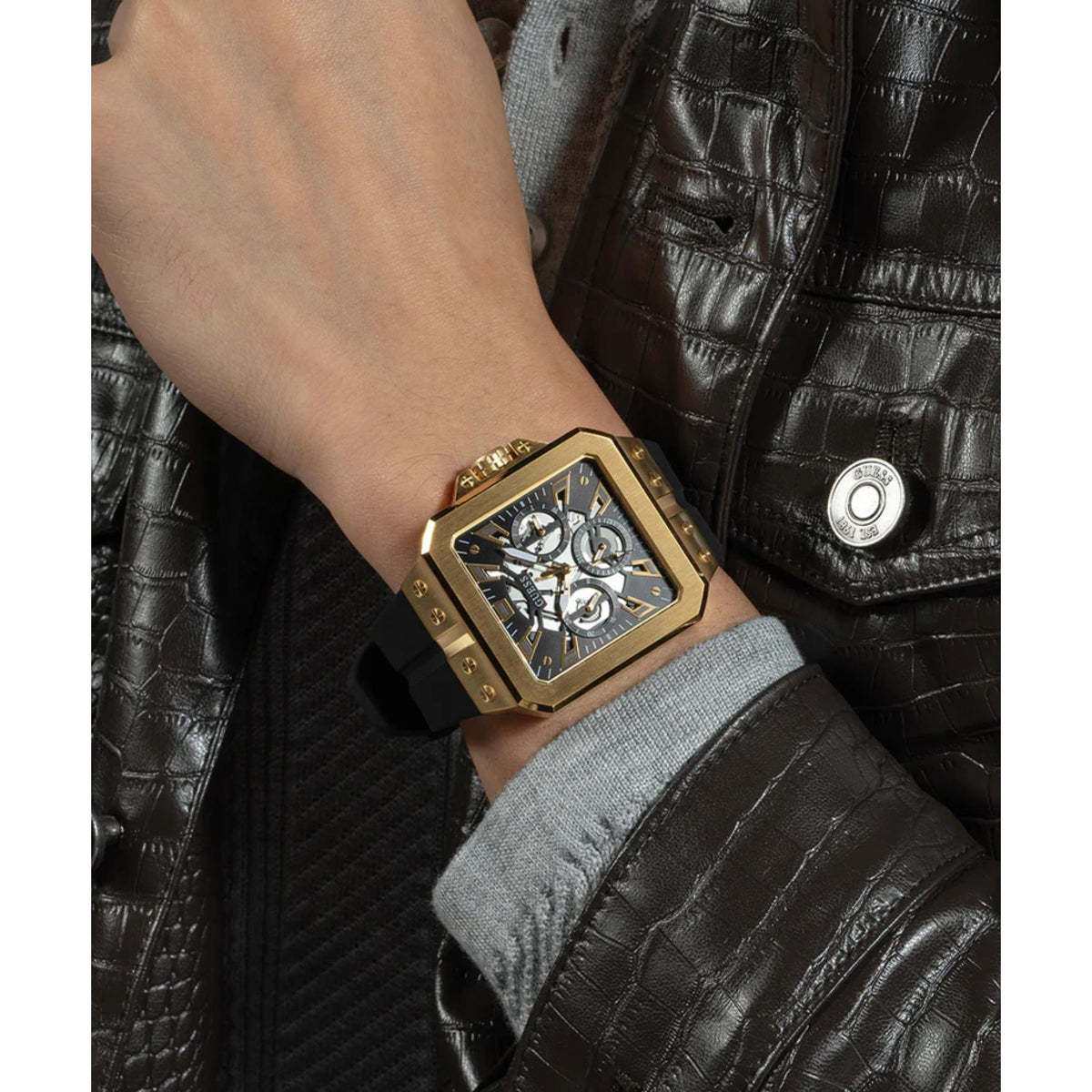 Men's Guess Leo watch on wrist, black dial and gold-tone case with black silicone strap