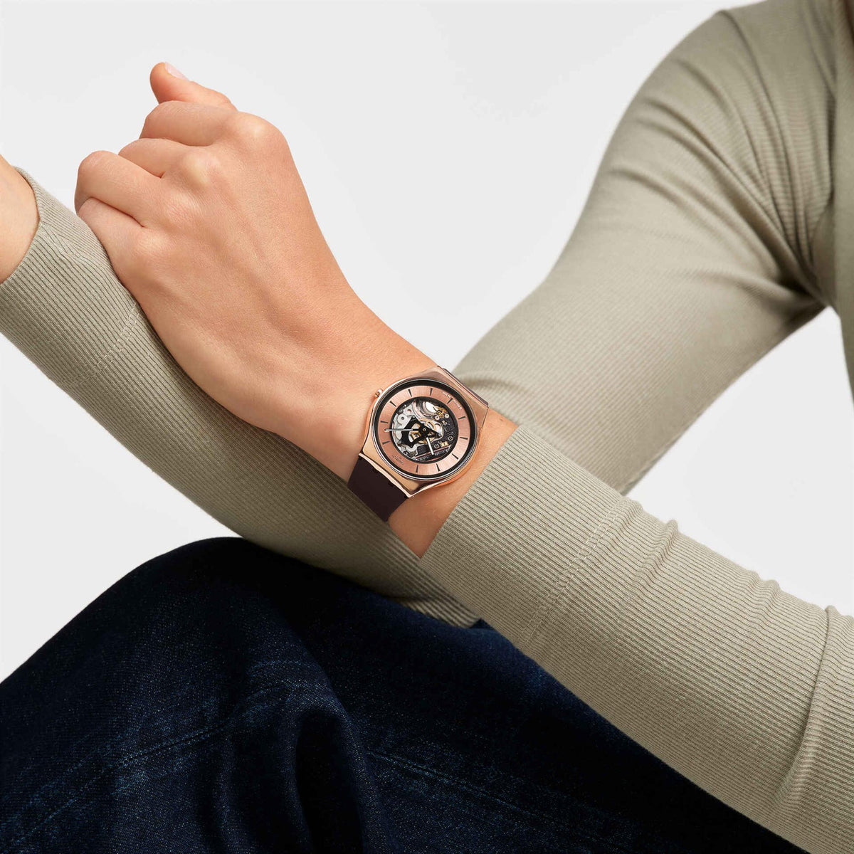 Copper-tone skeleton dial watch with dark silicone strap worn on wrist