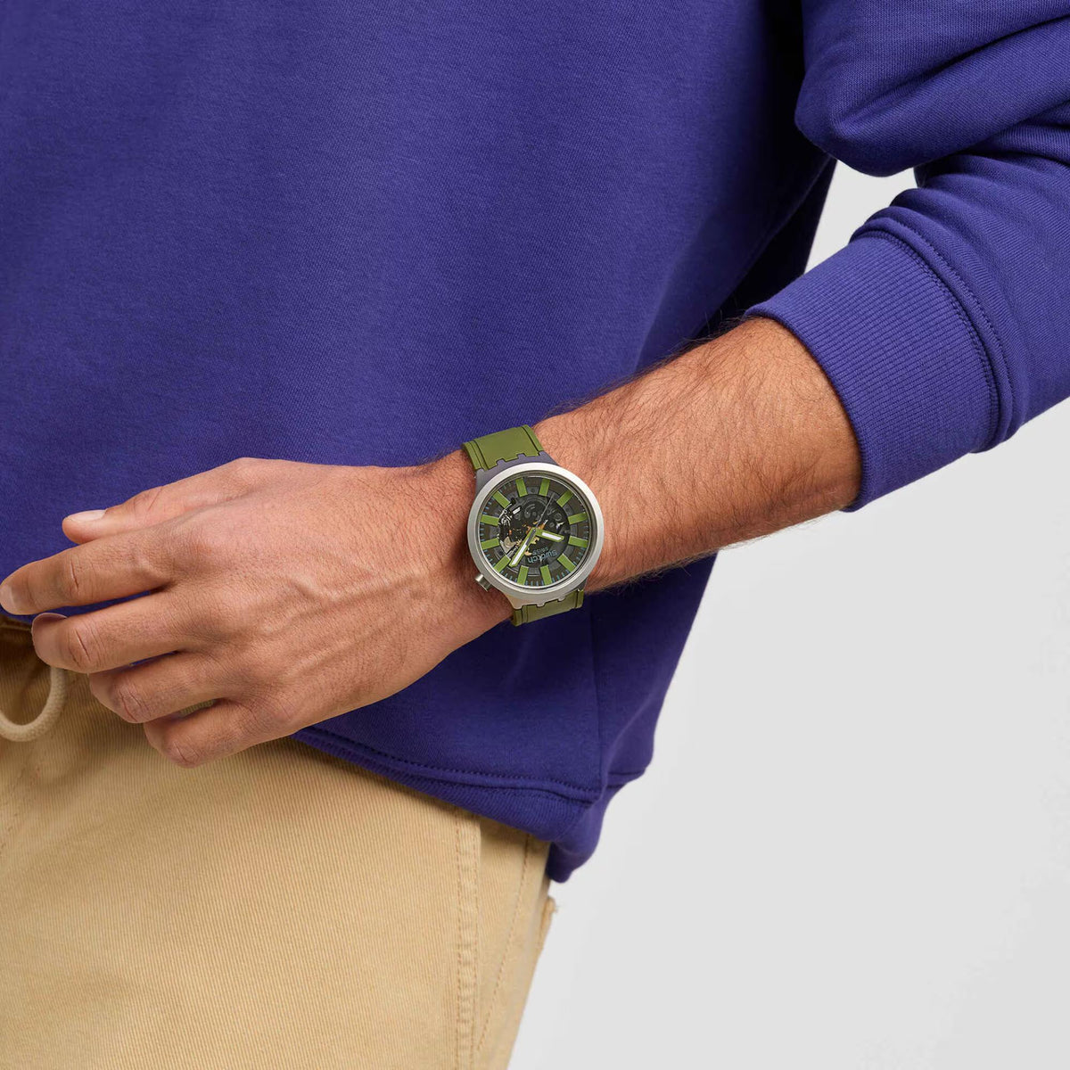 Swatch watch on wrist: green silicone strap and round black skeleton dial with neon accents