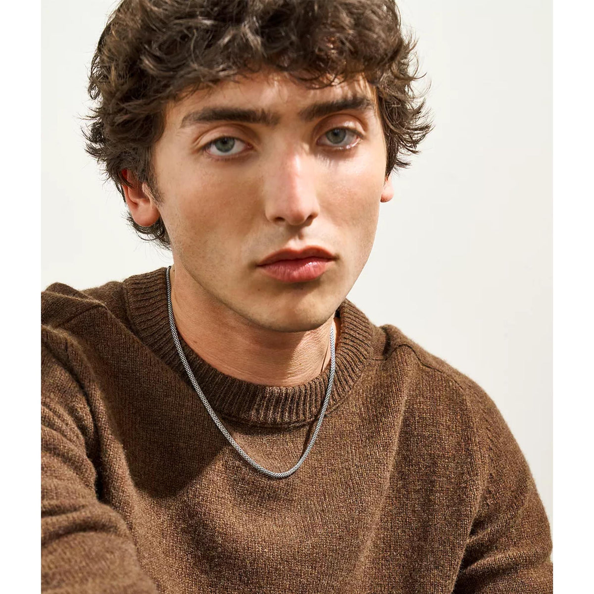 Silver chain necklace worn under brown knit sweater at the collar