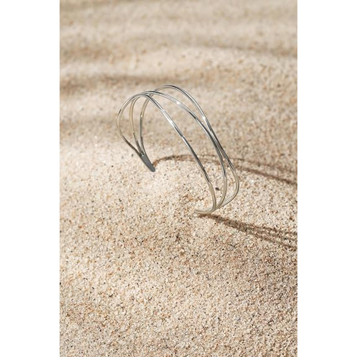 Silver-tone wire bracelet shown from side on sand, three curved bands open cuff