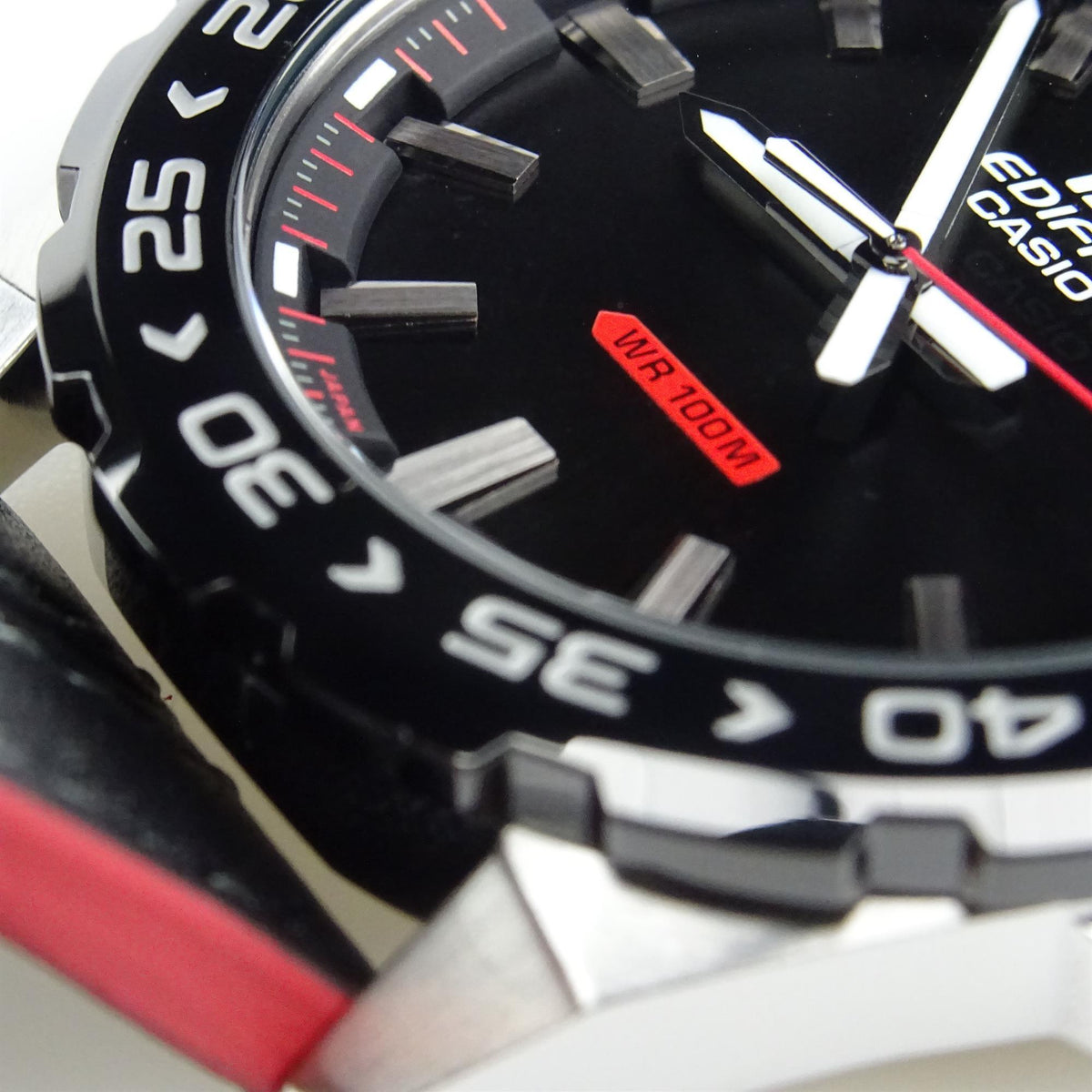 Men's wristwatch close-up: black dial, red-trim hands, WR 100M label, black leather strap