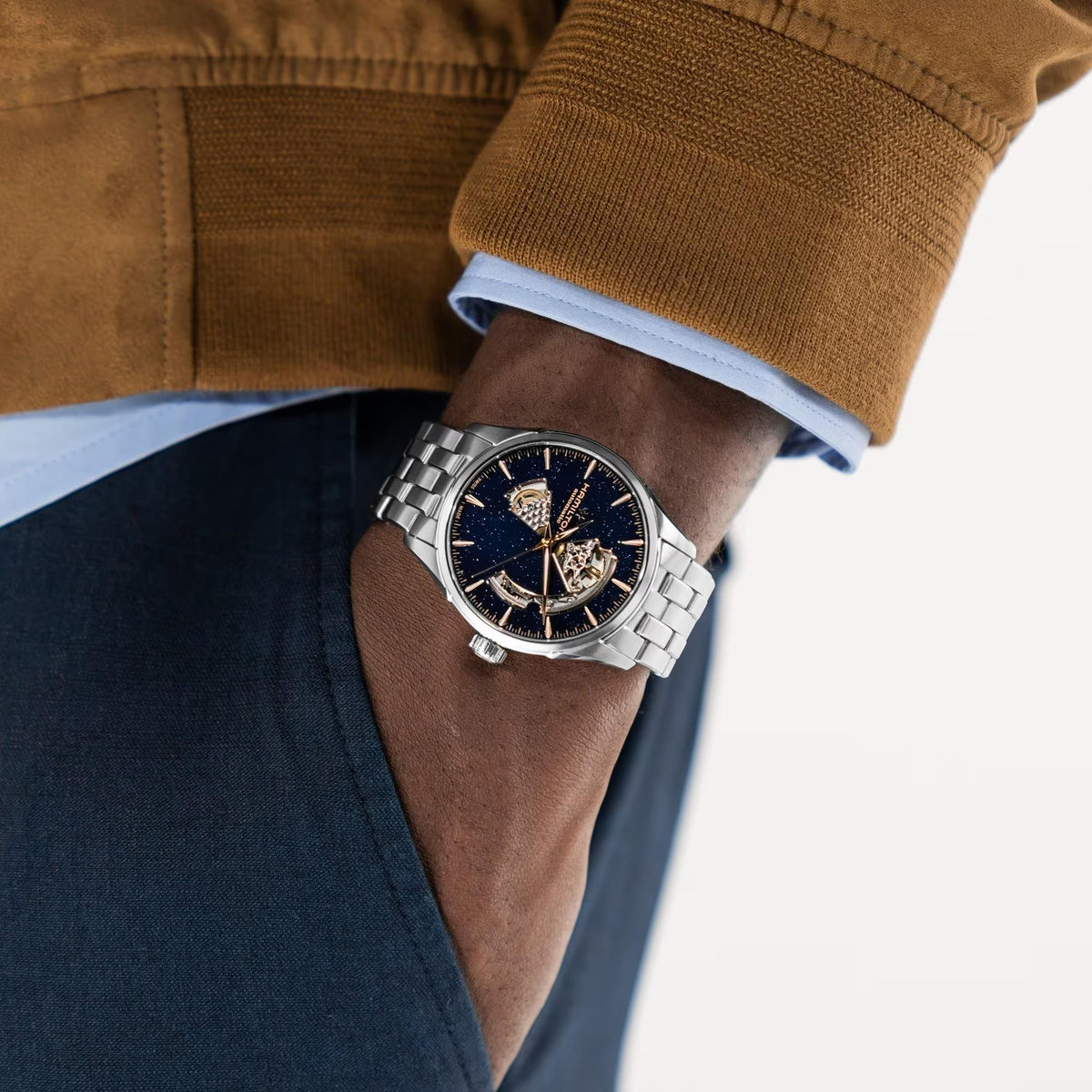 Hamilton Jazzmaster Open Heart H32705140 mens automatic watch lifestyle wrist shot paired with a brown jacket displaying a blue dial