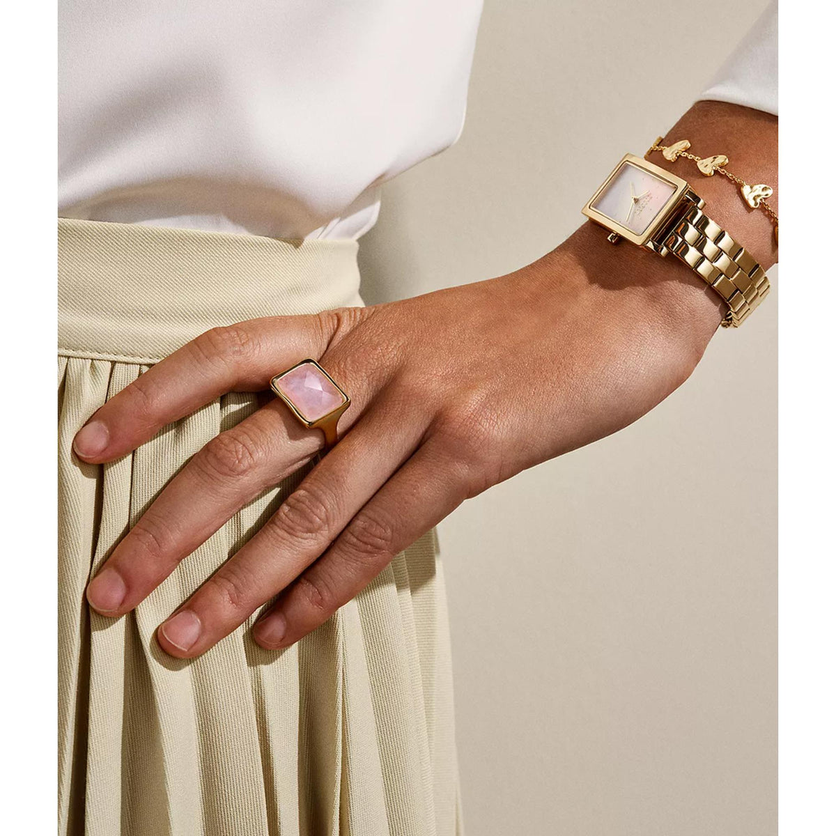 Gold-tone ring on finger with pink square faceted gemstone bezel