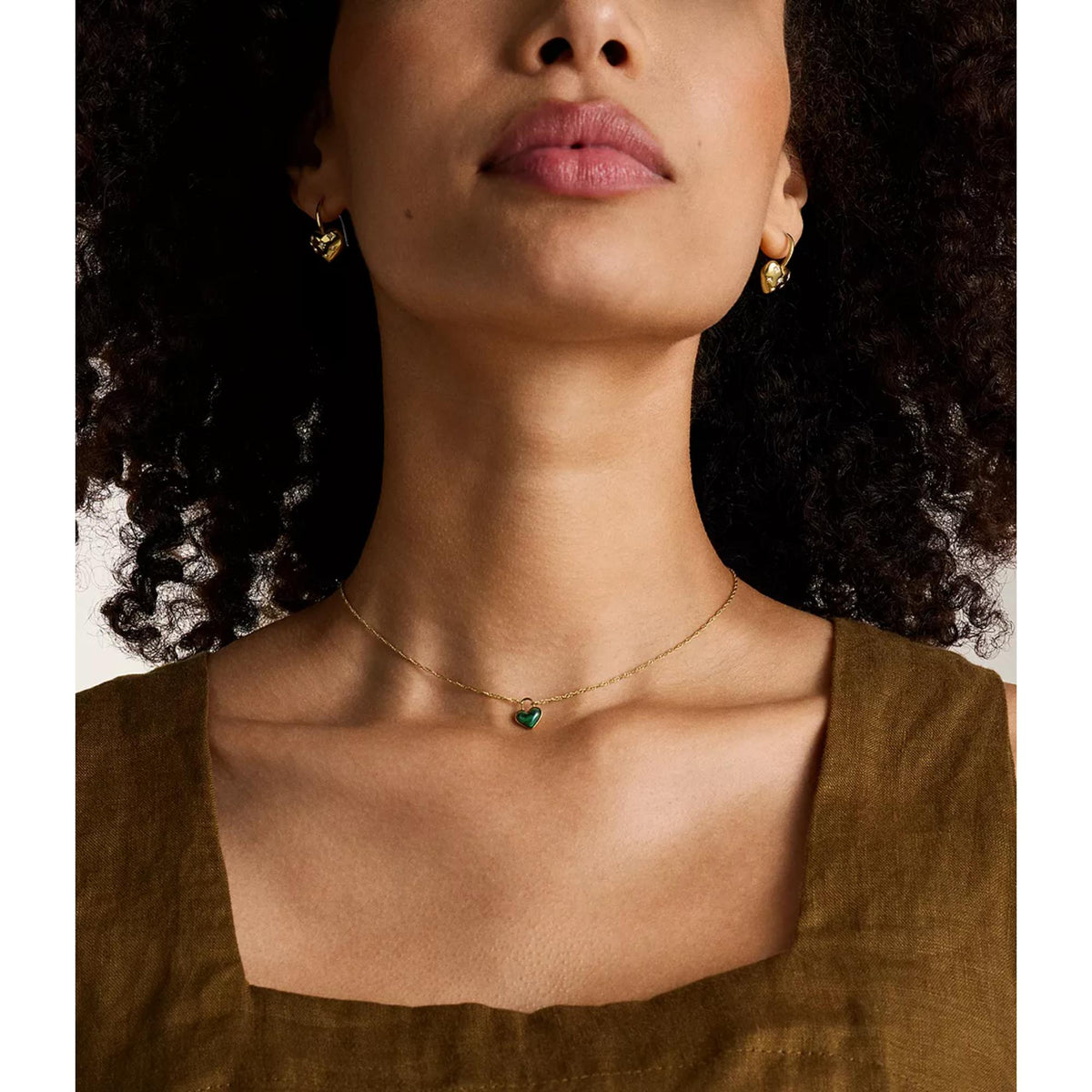 Model wearing gold-tone heart drop earrings with starburst details; small hoop hooks shown.