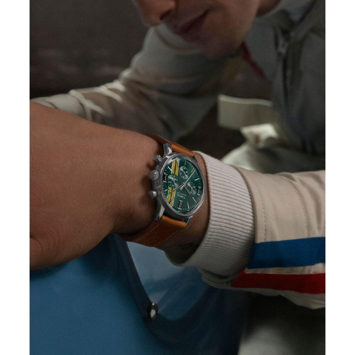 Men's wristwatch with green dial and brown leather strap worn with light sweater