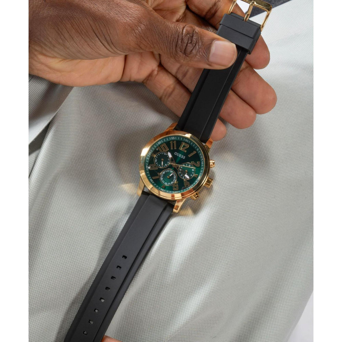 Men's watch with black silicone strap held up; green dial and gold-tone case visible