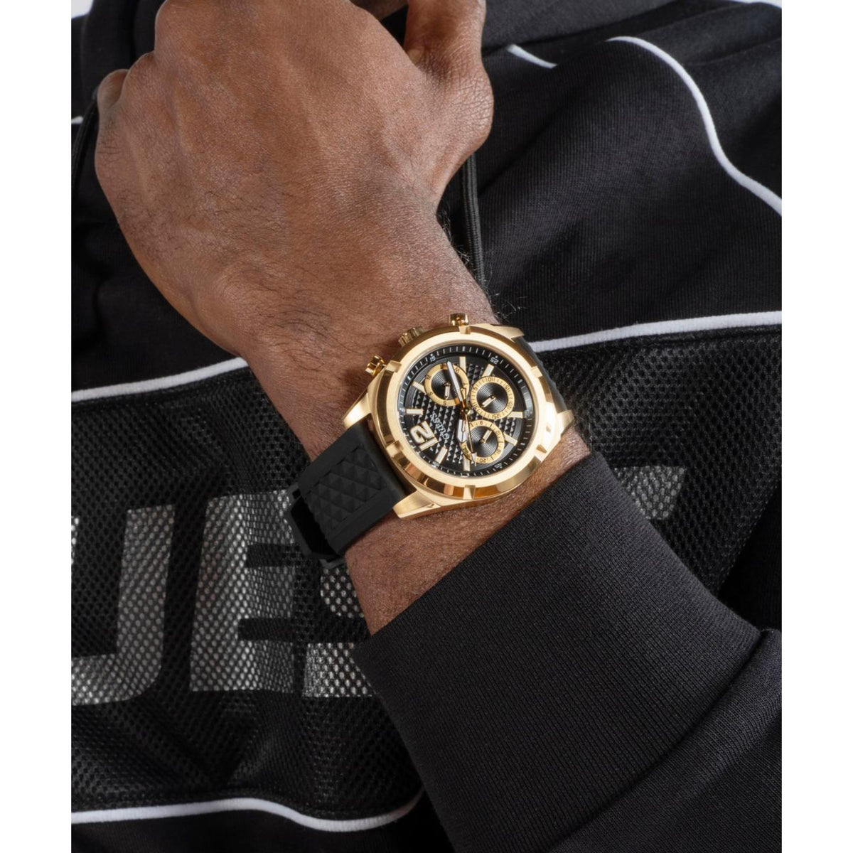 Men's gold-tone watch with black dial and black silicone strap worn on wrist.