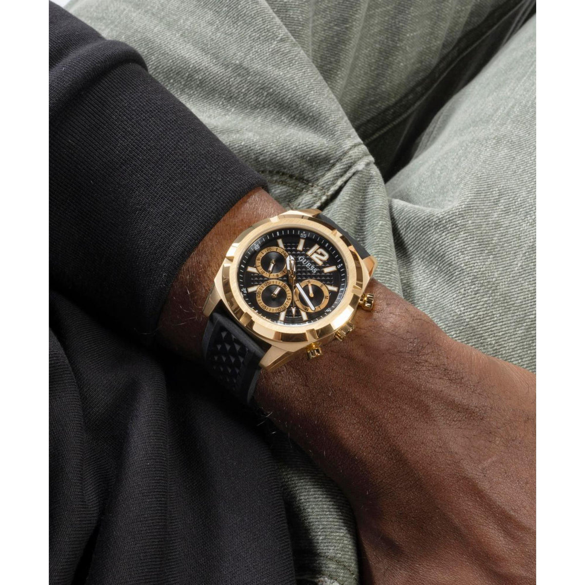 Men's gold-tone chronograph watch with black dial and black silicone strap on wrist.