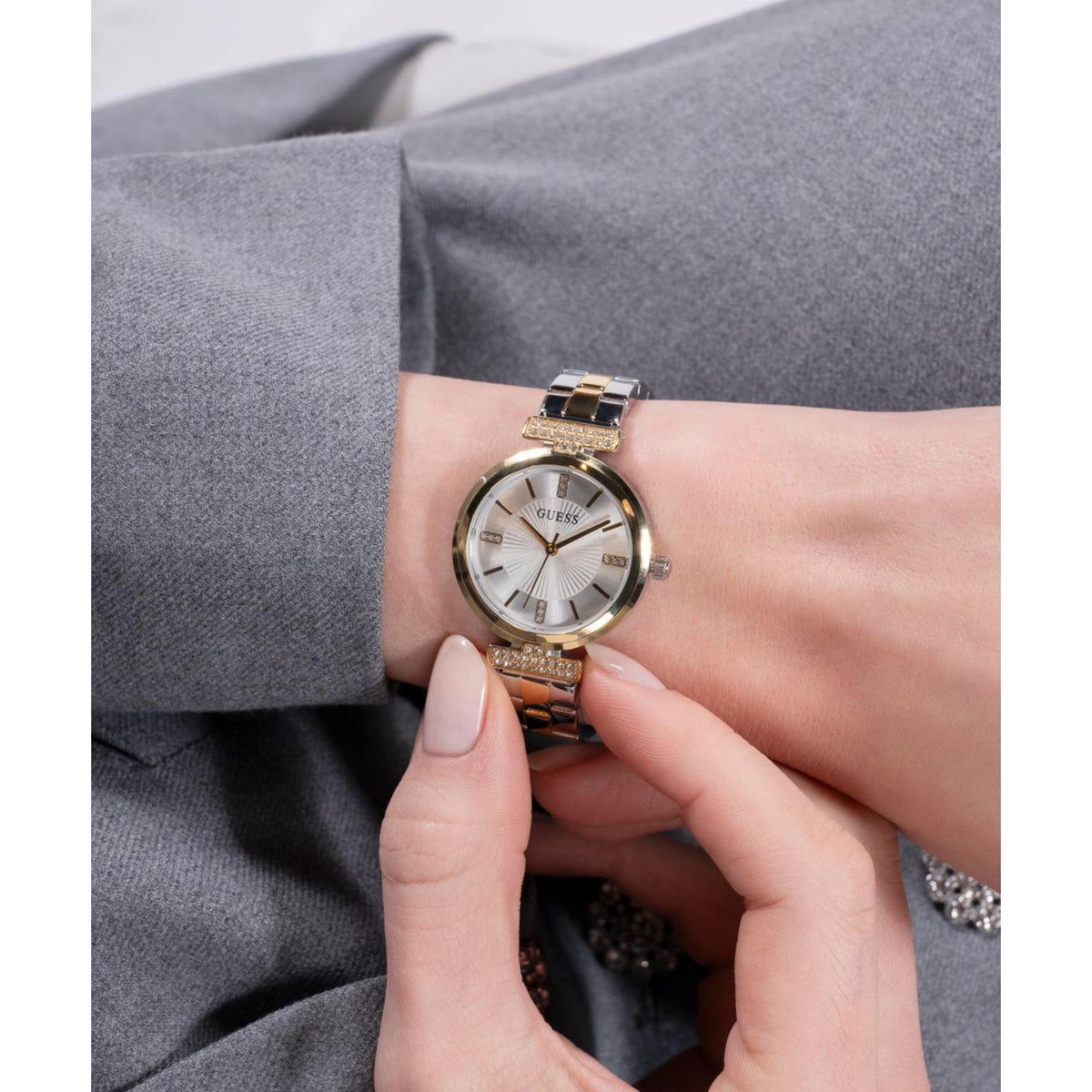 Guess women’s two-tone watch on wrist with white dial, gold details, and crystal accents