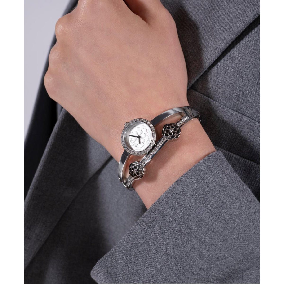 Women’s silver watch on wrist with round white dial and textured floral links
