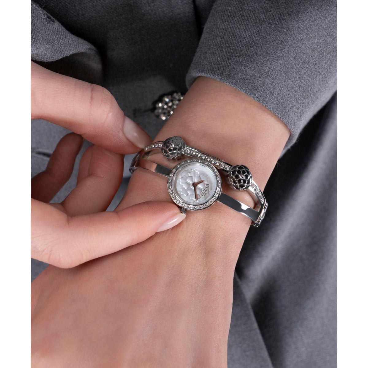 Women’s silver watch close-up on wrist with white dial and textured floral link accents