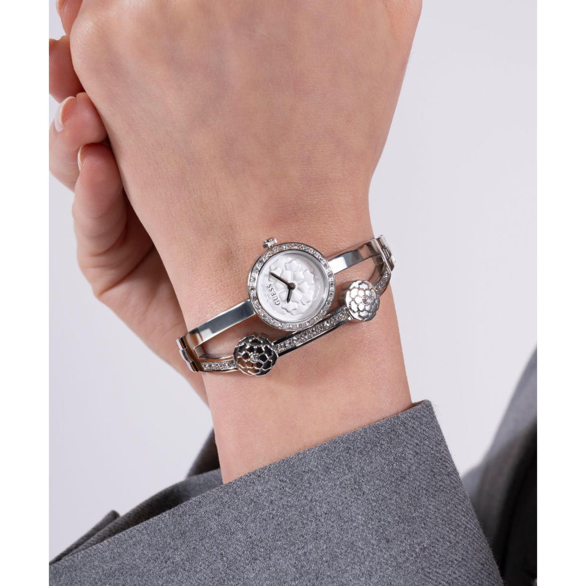 Women’s silver stainless steel watch with round white dial, bezel stones, and floral cuff links