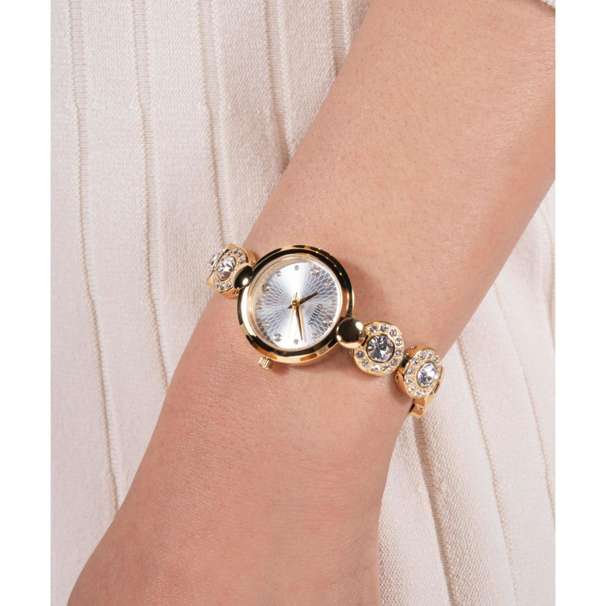 Women’s gold-tone watch on wrist with white dial and rhinestone bracelet links