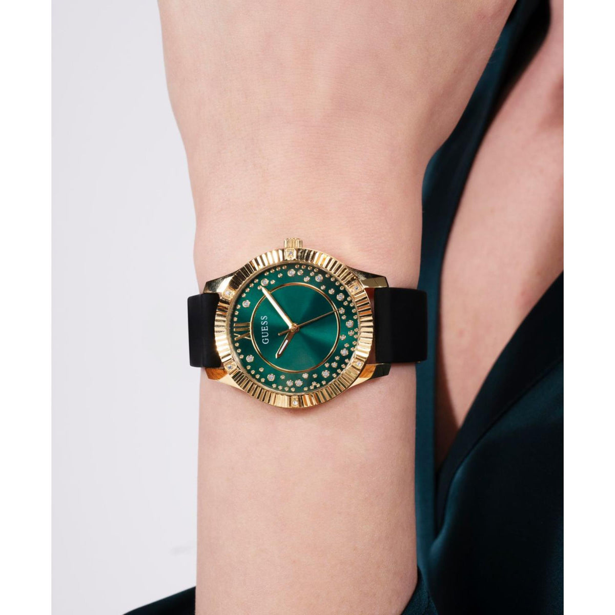 Guess women's watch on wrist, green dial with gold-tone bezel and black silicone band