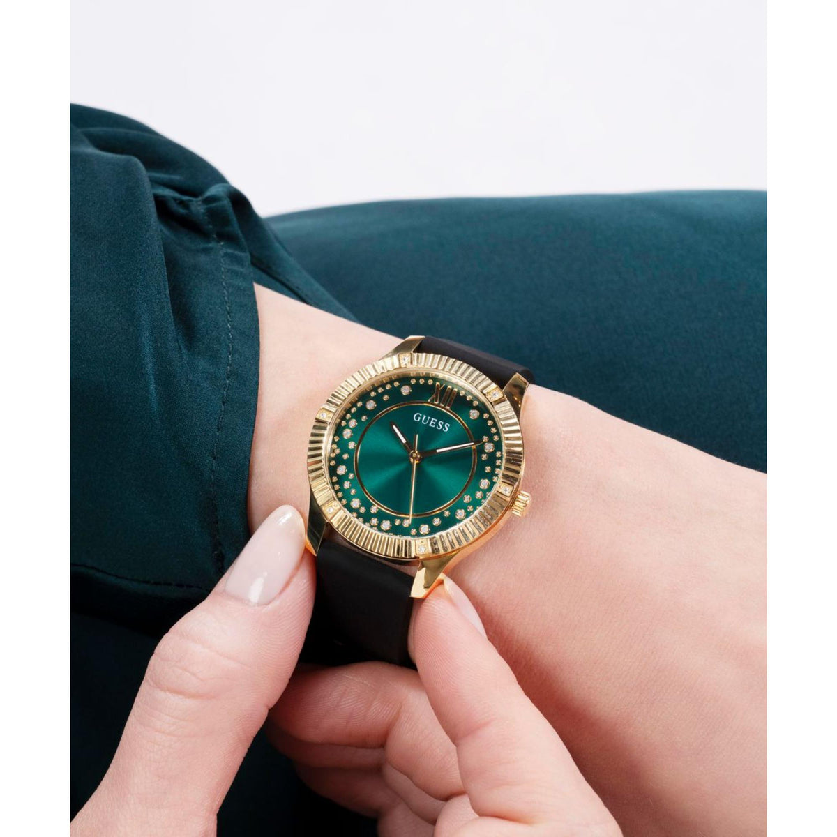 Guess women's watch on wrist, black silicone strap with gold-tone case and green dial
