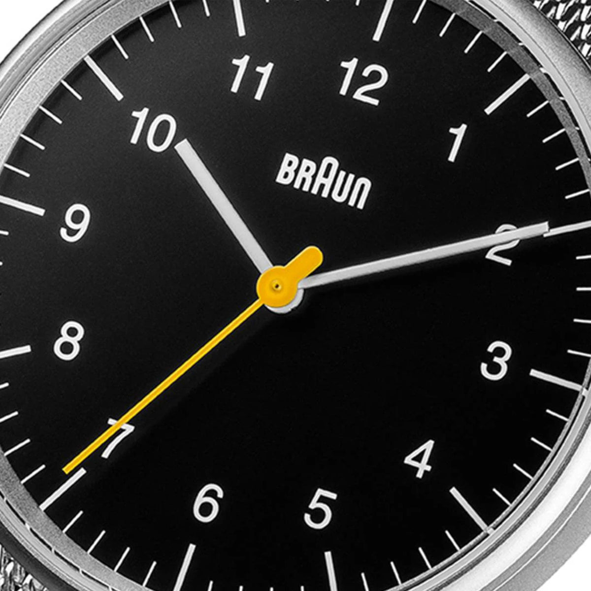 Men's watch close-up: black dial with Braun logo, white indices, yellow minute hand
