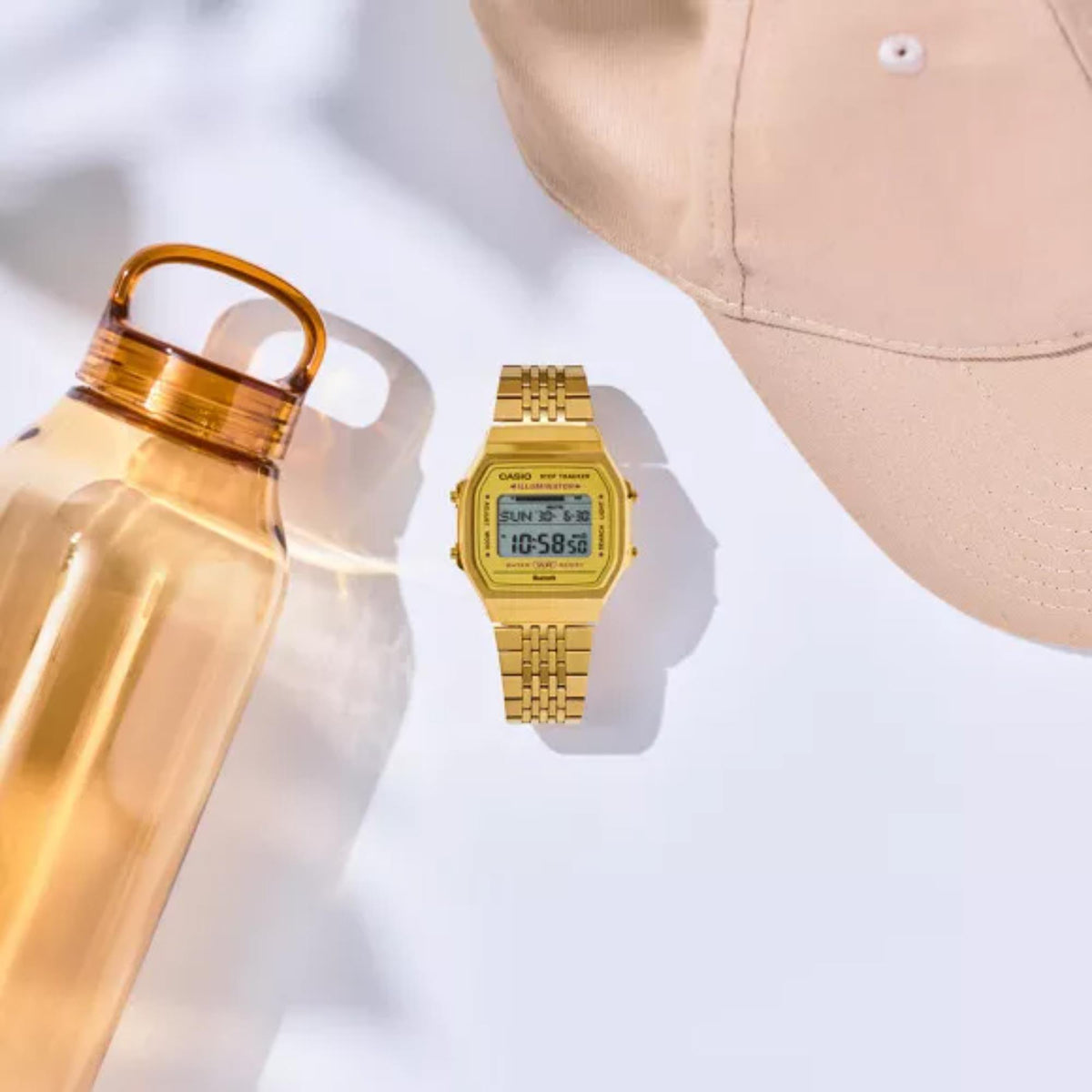 Flat lay arrangement of the gold Casio Vintage Digital Steel Strap Watch ABL-100WEG-9AEF alongside a water bottle and cap