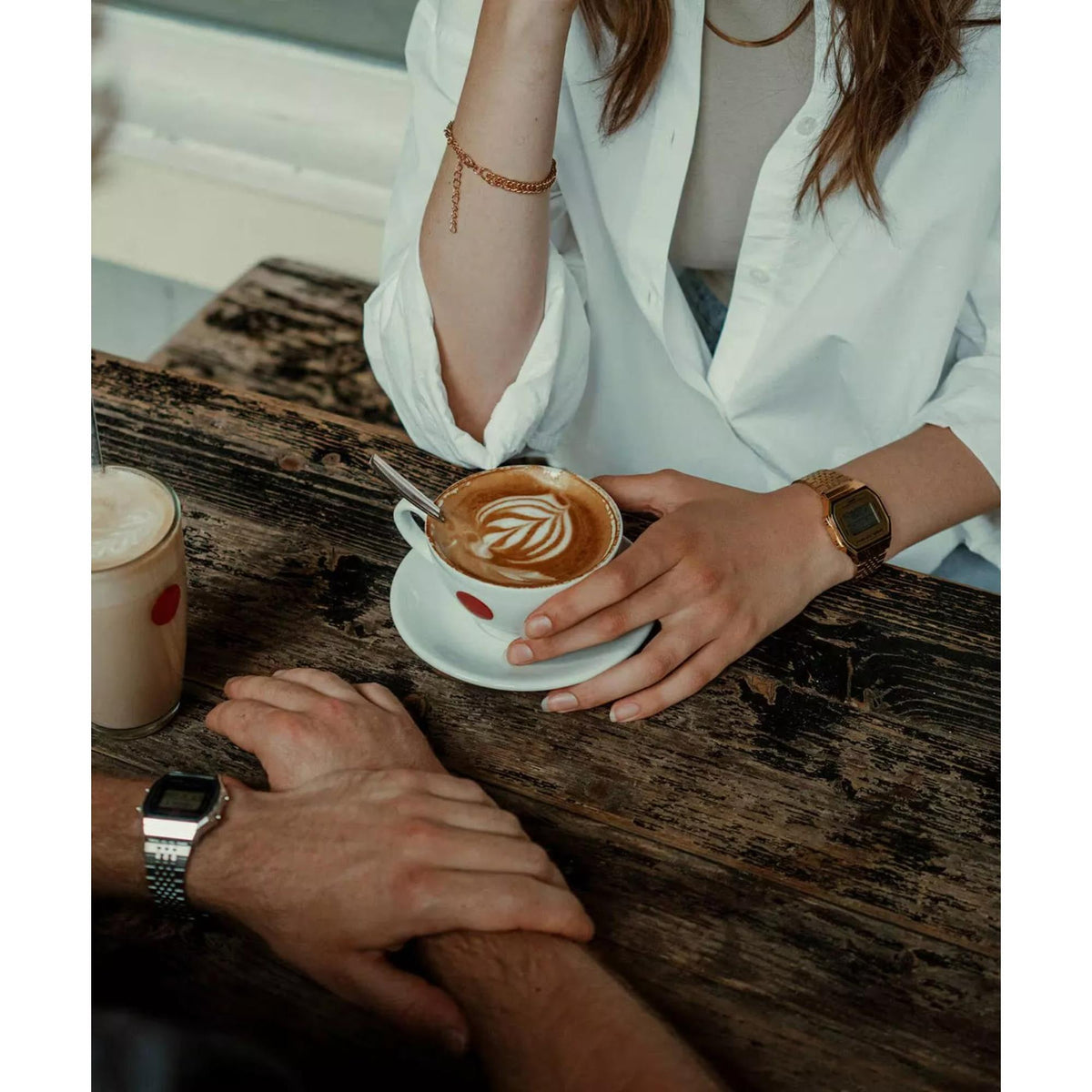 Café setting lifestyle shot of a woman wearing the Casio Vintage Digital Steel Strap Watch ABL-100WEG-9AEF while holding a coffee cup