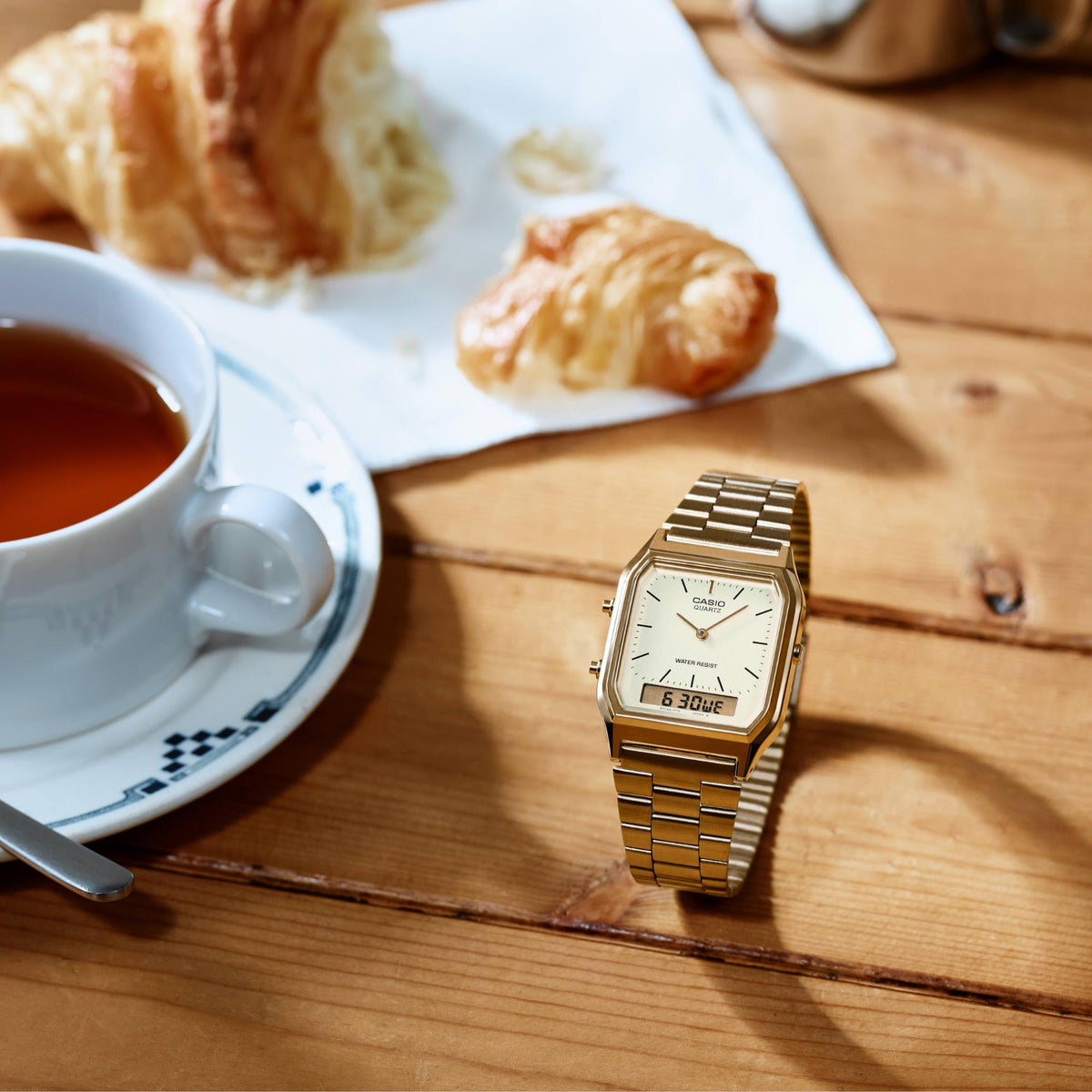 Casio Collection Vintage AQ-230GA-9DMQYES on a wooden table next to a teacup and croissants, emphasizing its retro aesthetic