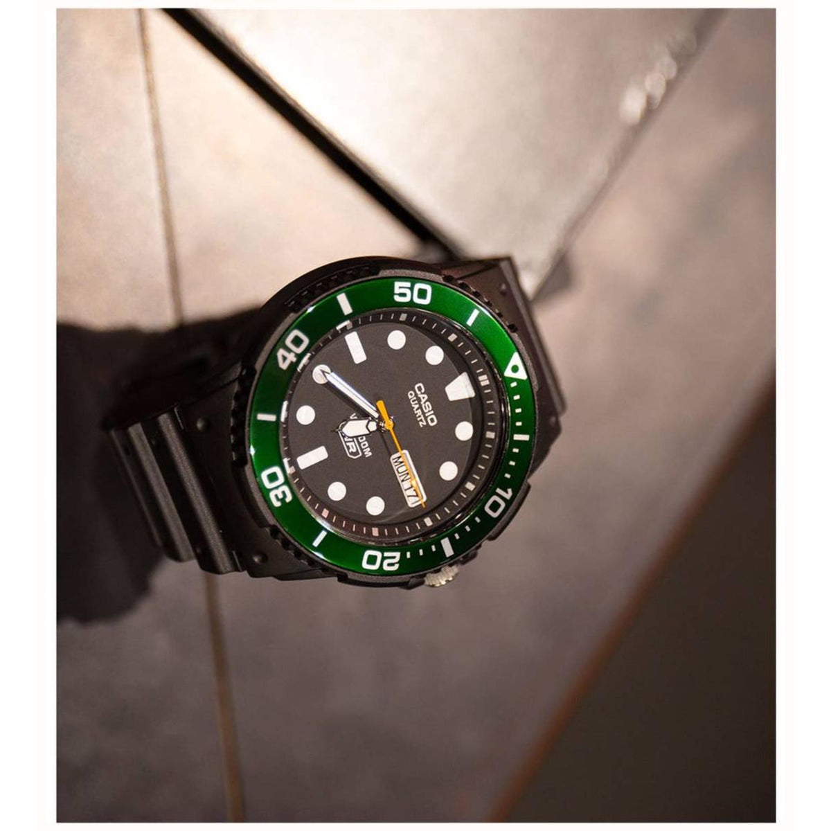 Angled view of the Casio Vintage Diver MRW-230H-1E3VEF quartz watch displaying its green bezel, black dial, and day-date window on a dark surface