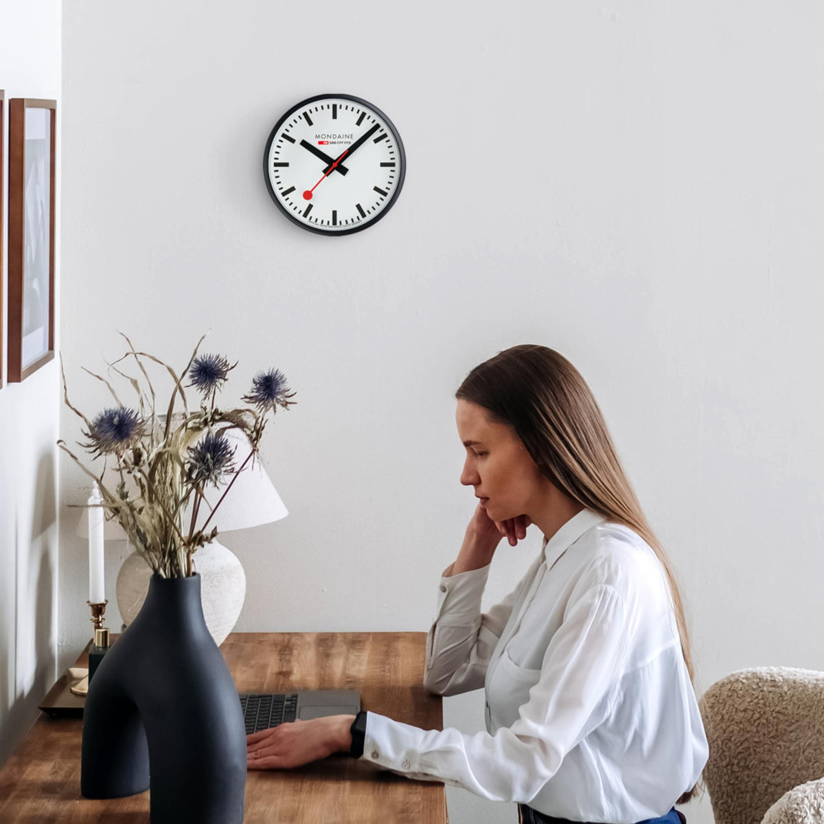 Mondaine quartz wall clock A990.CLOCK.12SBB styled above a wooden study desk setup