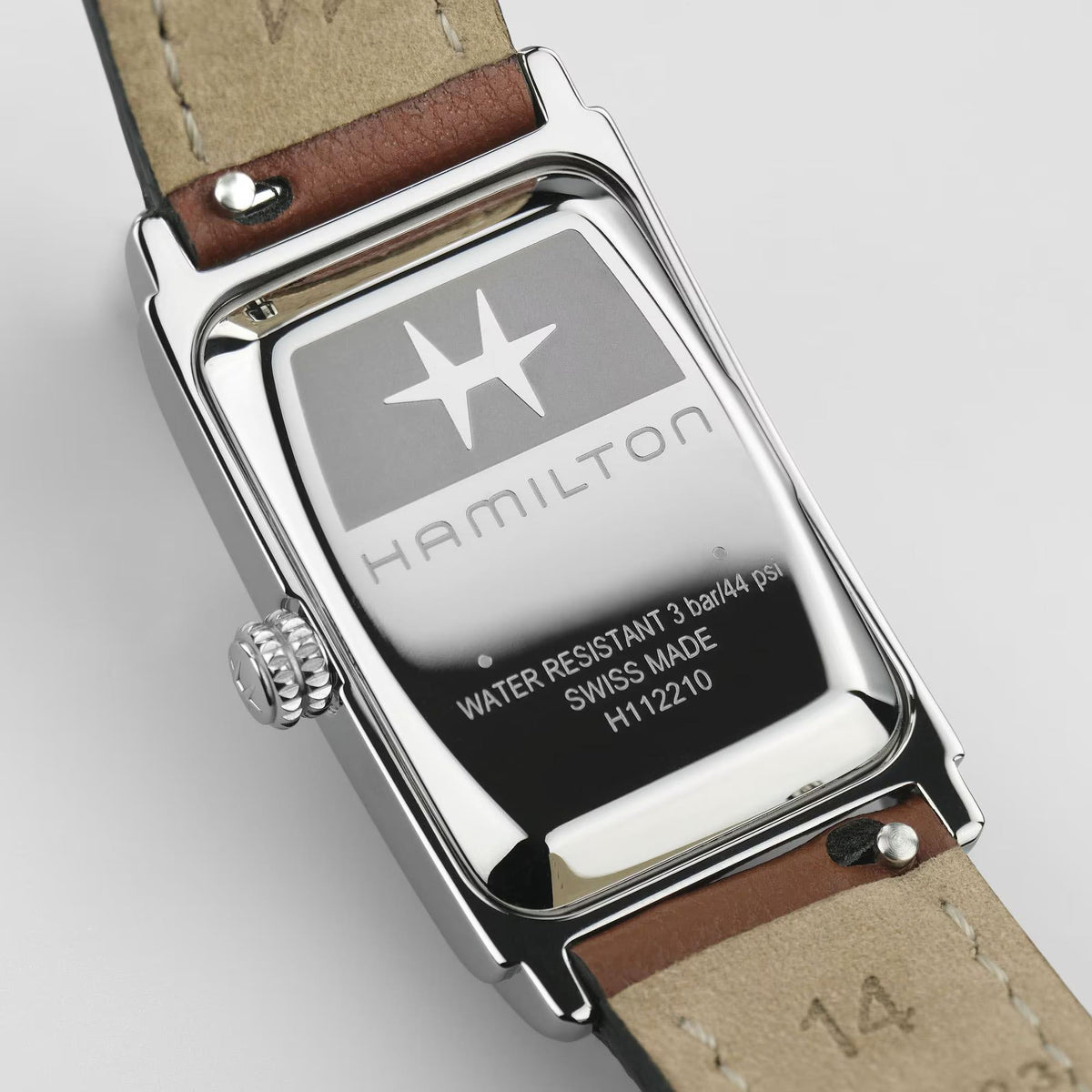 Stainless steel caseback with text on brown leather strap, square watch