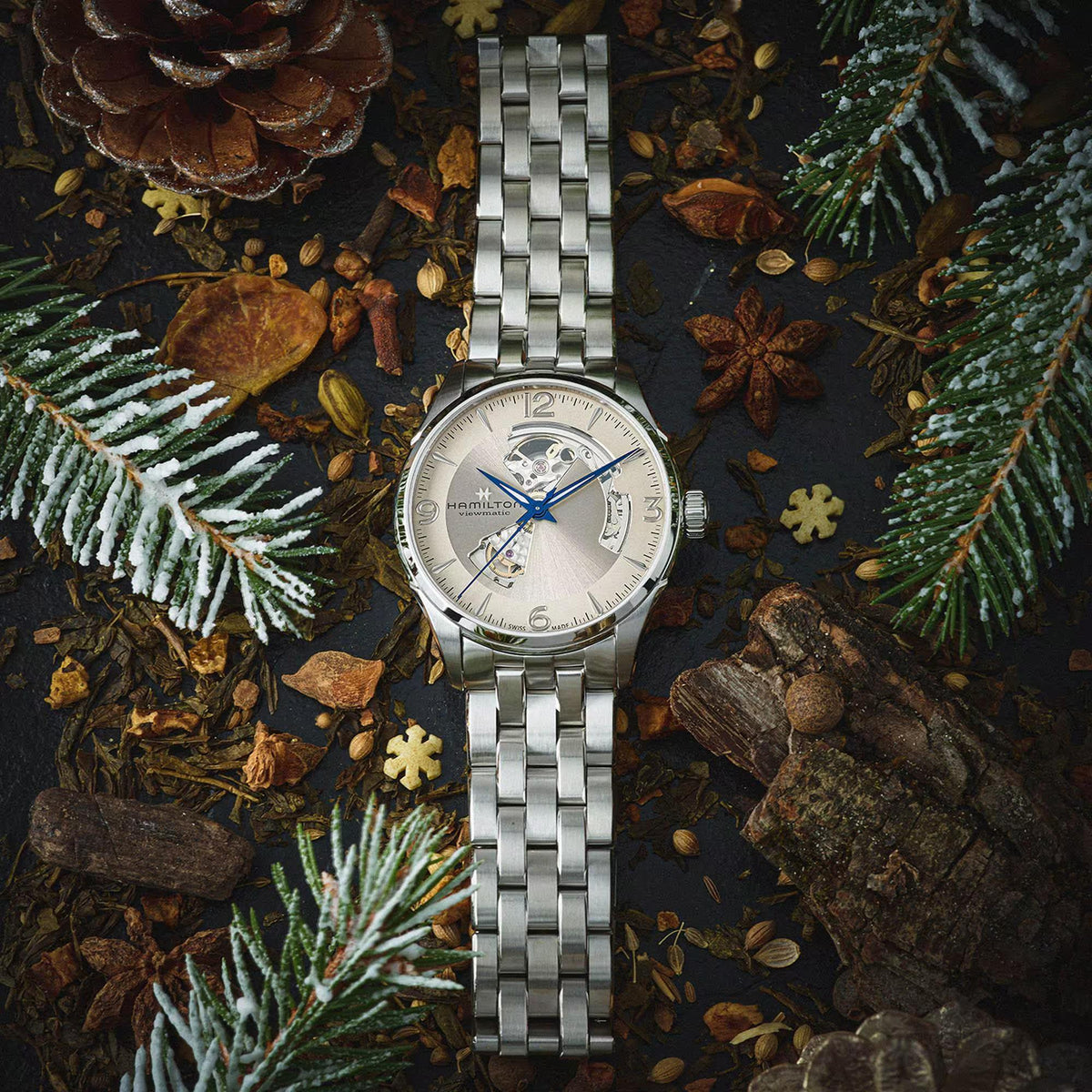 Hamilton Jazzmaster H32705121 automatic watch flat lay view surrounded by festive pine branches displaying beige dial and steel strap