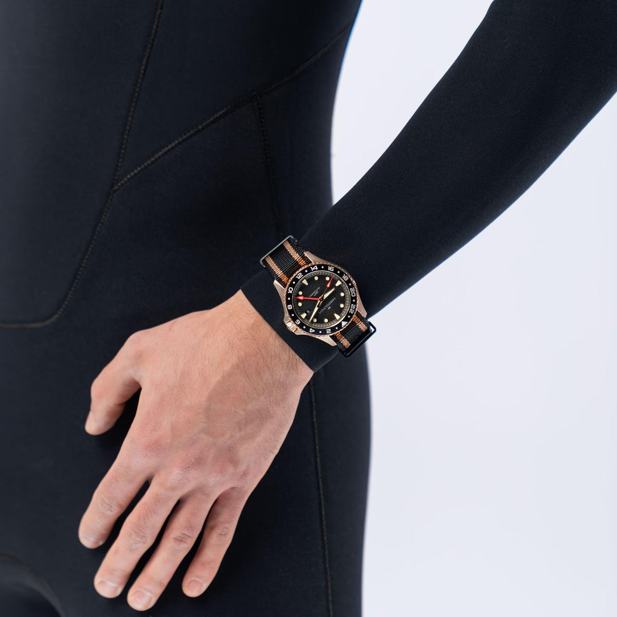 Wristwatch with black dial and brown striped NATO strap on a model's wrist