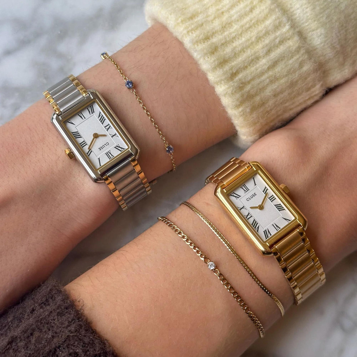 Two-tone steel watch with white dial and Roman numerals worn with jewelry bracelets