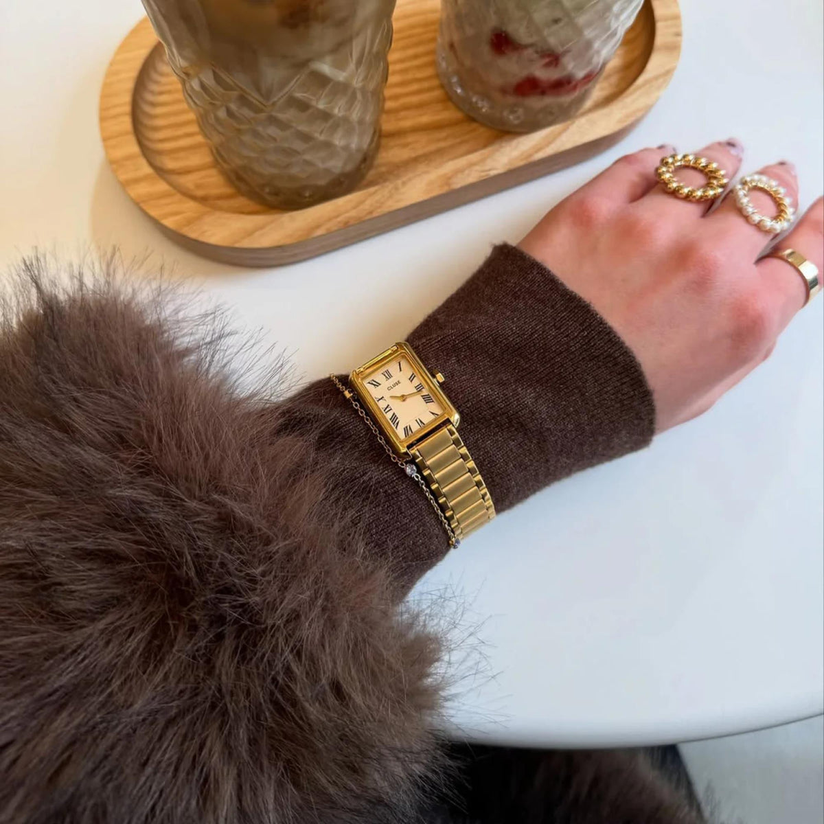 Gold-tone rectangular watch with white dial on wrist