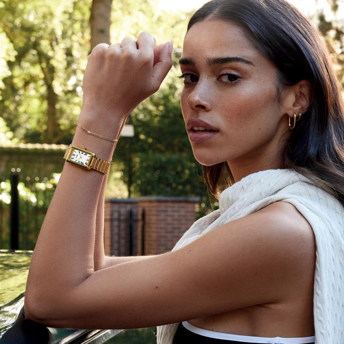 Gold-tone rectangular watch with white dial and Roman numerals on wrist
