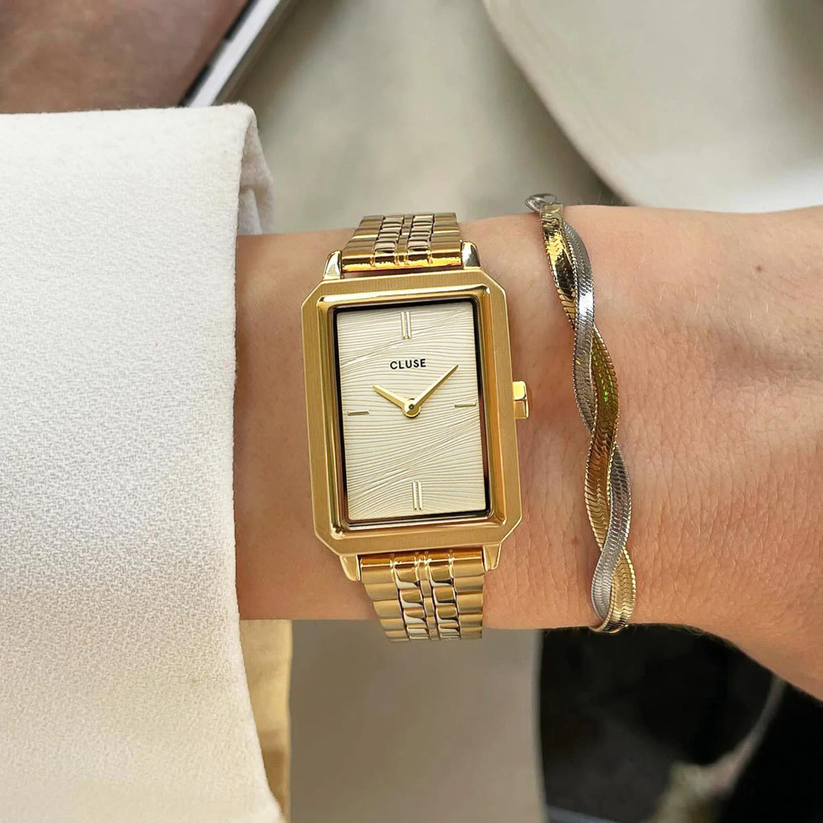 Gold square quartz watch with cream dial and metal link bracelet on a wrist