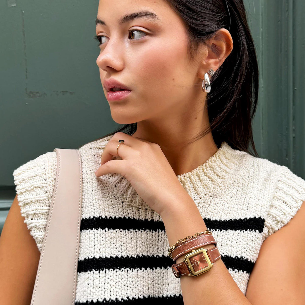 Square watch with brown leather strap and gold-toned case on wrist, sweater visible